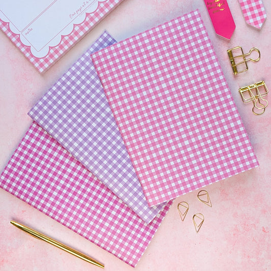 Pink and purple checkered paper sheets with gold clips on a pink background
