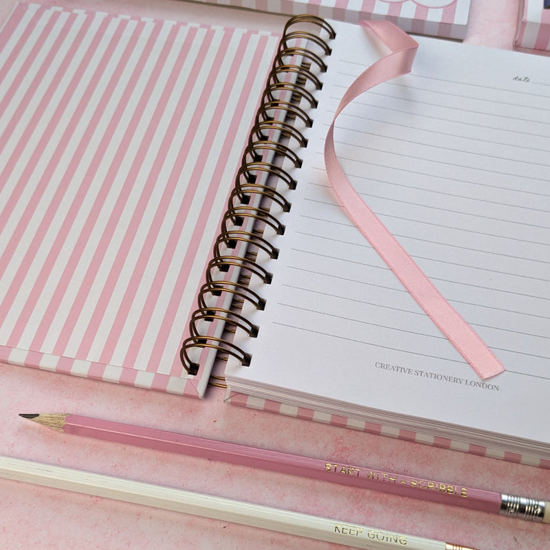 Notebook with pink and white striped cover and a pink pencil on a matching background