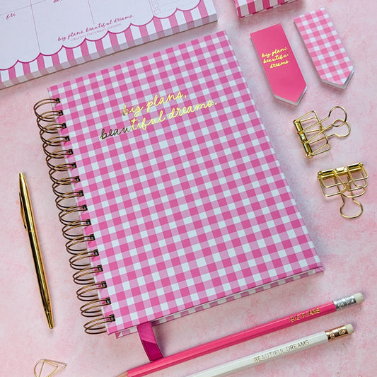 Pink checkered notebook with 'big plans, beautiful dreams' text on a pink background with stationery items.