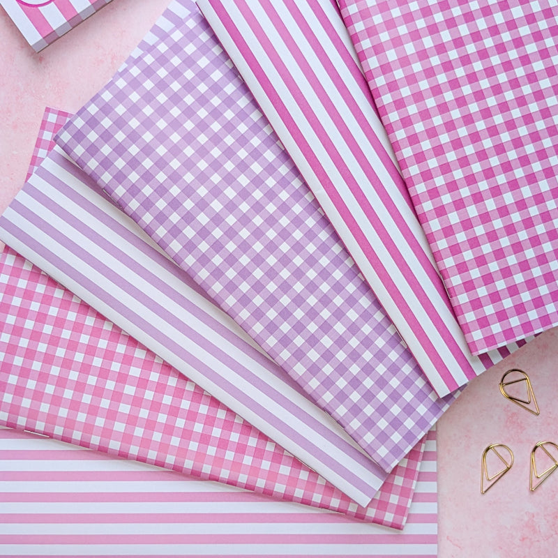 Pink and white checkered and striped paper sheets on a pink surface with heart-shaped objects.