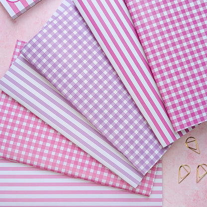 Pink and white checkered and striped paper sheets on a pink surface with heart-shaped objects.