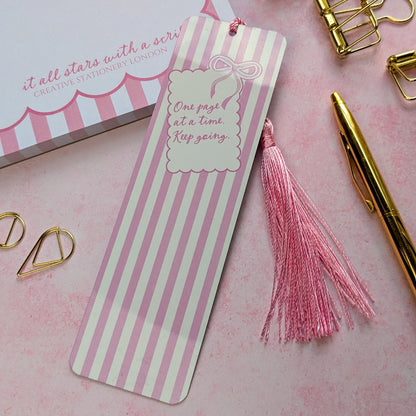 Striped bookmark with pink tassel on a pink background with stationery items.