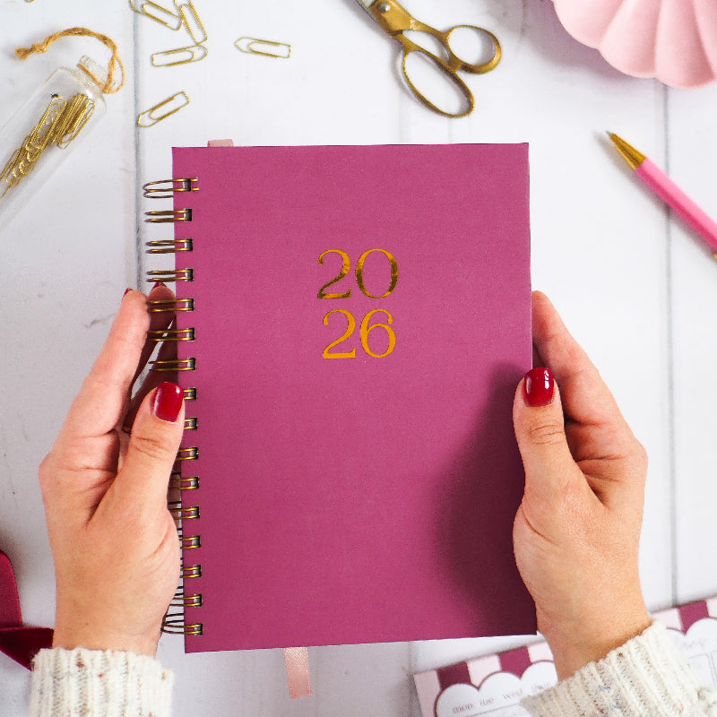 Burgundy planner with '2026' in gold foil on a white surface with stationery items